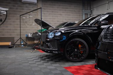 Parlak siyah Bentayga Speed kapalı bir garajda, matris ızgarası, kristal kesimli LED farlar, siyah alaşımlı tekerlekler ve turuncu fren kalibreleri ile park edilmiş..