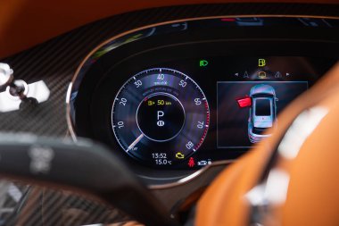 Yakın iç görüntü Bentley Bentayga Hız Kümesi 'nin Park' ta olduğunu gösteriyor. 50 km / h hız sınırı uyarısı. Üst kapı aralığı sol arka, saat 13.52, 15.0 C, karbon fiber ve turuncu deri..