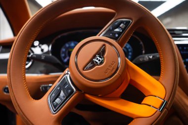 Bentley Bentayga Hız Direksiyonunun yakın görüntüsü, Kanatlı deri ve hava yastığı kabartması, kürekli vites ve yumuşak dijital küme parıltısı..