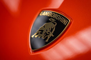 Yakından bakınca parlak turuncu paneldeki Lamborghini armasını görüyoruz. Yumuşak yansımalar ve sığ alan derinliği metalik süslemeyi ve incili boyayı vurguluyor.