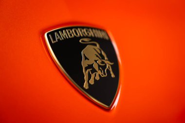 Yakından bakınca turuncu gövde panelinde Lamborghini armasını görüyoruz. Amblem parlak yansımalarla ve bir stüdyoyla net bir şekilde odaklanmış..