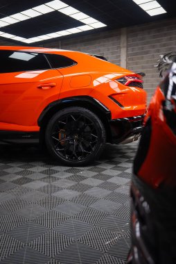 Yakından bakınca turuncu Lamborghini Urus SE 'yi bir atölyede gösteriyor. Keskin stop lambaları, siyah çoklu konuşma tekerlekleri, turuncu kalibreler ve rozetler dikkat çekiyor..