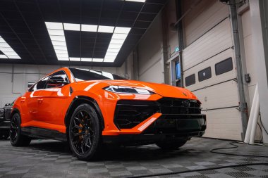 Bir atölyede Lamborghini Urus SE 'nin düşük açılı görüntüsü, floresan tavan panelleri ve garaj kapıları, tekerlekler ve LED farlar görünür..