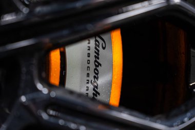 Yakın çekim çerçeveleri siyah alaşımlı bir tekerlek konuştu ve Lamborghini ve Carboseramic metin ile gümüş fren. Bir atölyede kapalı, karamsar yansıtıcı ışık metal ve su lekeleri gösterir.