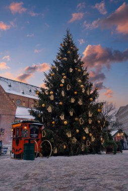 Altın süsler ve eldivenlerle bir Noel ağacı Riga Eski Kasabası 'nda duruyor. Akşam karanlığında Kubbe Meydanı yakınlarında. Yakınlarda tuğla cepheli bir dükkan var..