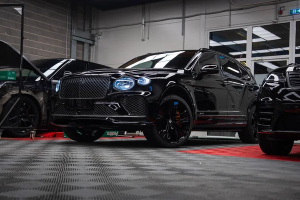 Parlak siyah Bentley Bentayga Speed kareli zeminde oturuyor, matris ızgara ve oval LED farlar görünür, siyah tekerlekler, kırmızı kalibreler, aletler ve duvarlar garaj ayarlarını gösteriyor.