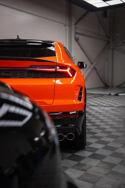 Üçte üçü turuncu Lamborghini Urus SE 'yi açısal LED arka lambası, dört egzoz ucu, kareli zemin ve üstten floresan ışıkları olan bir atölyede gösteriyor..