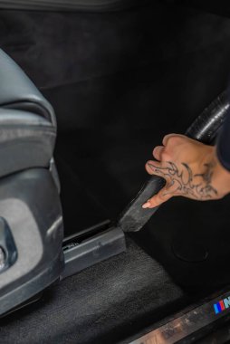 Arabanın içini kapatın. Koltuk raylarının kenarlarını süpüren dövmeli bir el görünüyor. BMW M üç renkli kapı pervazı görünür, yumuşak hatta aydınlatma ve yüzeysel alan derinliği detaylara odaklanıyor..