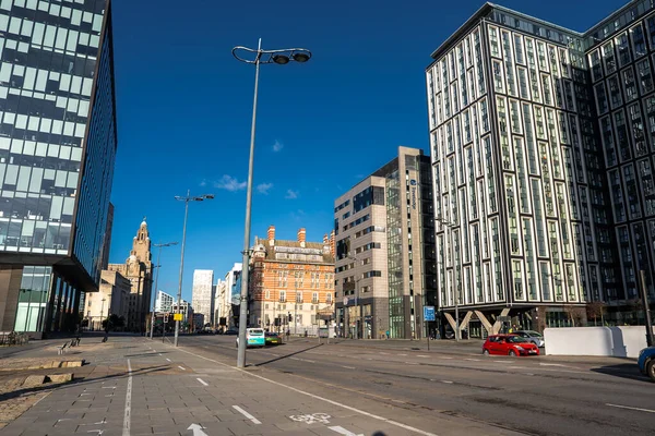 Modern kuleler ve Liverpool 'da kırmızı tuğlalı Victoria tarzı bir bina standı. Arabalar ve taksiler bisiklet yolunun yanında hareket ediyor. Liverpool Limanı saat kulesi solda..