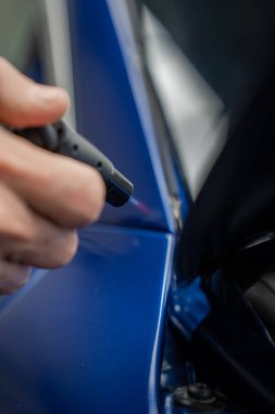 Bir teknisyen, galeri servis hangarındaki parlak mavi lüks bir arabanın ısı kalemi boyunca hareket ettiriyor. Yumuşak ışıklandırma titiz bir detay ve metalik bir bitişi ortaya çıkarır.