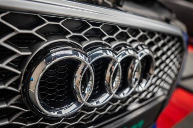 Audi ızgarasının dar bir görüntüsünde dört halka amblemi ve siyah ağ görünüyor. Atölye ışıklarının yansımaları, detaylandırma ve boya düzeltmesi yapılmakta olduğunu gösteriyor.