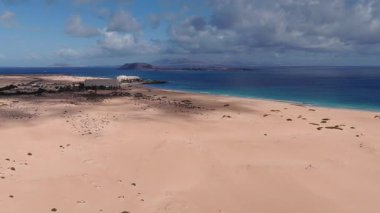 Hava manzarası, Corralejo, Fuerteventura 'nın altın kum tepeleri, oteller, şemsiyeler ve tekneleri gösteriyor. Lanzarote siluetleri ufukta oturuyor dalgalar kumlu kıyıya vururken.