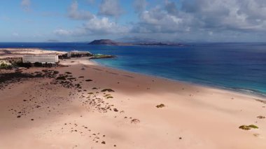 Fuerteventura, Corralejo yakınlarındaki kumsal ve altın kum tepelerinin hava manzarası. Resort 'lar kum tepelerinde oturur, Lobos ve Lanzarote ufku işaretler, dalgalar ve bulutlar yavaşça hareket eder..