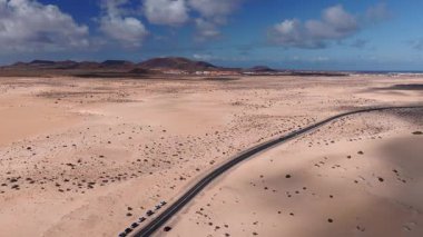 Fuerteventura kum tepelerinin, kavisli yolların, mavi arabaların, hareket halindeki araçların, volkanik tepelerin, ufuktaki Lanzarote 'nin hava gün ışığı görüntüsü..