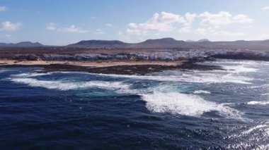 Fuerteventura şehrinin havadan görünüşü, beyazlatılmış oteller ve evler siyah lav kayaları, soluk kum tepeleri ve derin Atlantik sörfleri ile karşılaşıyor. Yollar, arabalar ve görülebilir dar bir plaj..
