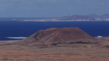 Fuerteventura, pas ve siyah lav dokuları, Atlantik kıyıları, sahil kasabası, gün ışığında Lanzarote 'de düz bir volkanik koni üzerinde hava aracı tepesi.