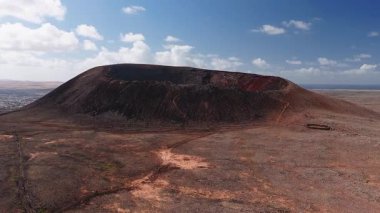 Fuerteventura, Kanarya Adaları 'ndaki büyük bir volkanik kraterin hava görüntüsü. Küçük bir sahil kasabası, okyanus, yuvarlak taş muhafaza ve patika yürüyüşçüleri görülebilir..