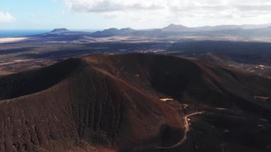 Havadan bakıldığında Fuerteventura 'da volkanik krater, lav alanları, Atlantik Okyanusu ve Lanzarote görünüyor. Akşamüstü ışıklarıyla kamera kenarın üstünde süzülüyor..