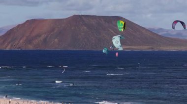 Fuerteventura 'nın kuzey kıyısı, Lobos Adası, kumlu plaj, turkuaz suya oyma yapan uçurtma sörfçüleri, küçük dalgalar, şemsiyeler, kıyıdaki insanlar..