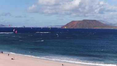 Fuerteventura, Corralejo yakınlarındaki hava manzarası. Montana Roja ve Lanzarote ufukta otururken uçurtmalar ve uçurtmacılar turkuaz ve deniz üzerinde uyanıyorlar..