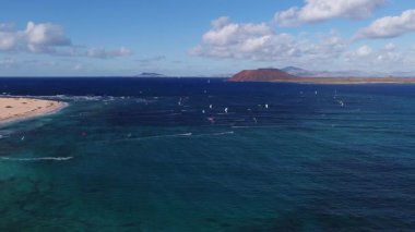 Hava günışığı sahnesinde Corralejo 'nun kum tepecikleri, kırmızı bir volkanik koni ve Lanzarote Atlantik dalgaları üzerinde uçan uçurtmalar gibi ufukta görünüyor..