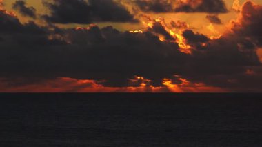Fuerteventura, Kanarya Adaları açıklarındaki 4K Atlantik Havayolları. Koyu kümüliform bulutları turuncu gündoğumuyla ya da günbatımıyla aydınlanır geniş ufuk ve okyanus boyunca kreusküler ışınlar oluşturur..