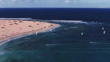 Fuerteventura 'nın gündüz görüntüsü ve turkuaz sığ kum tepeleri, derin Atlantik mavisi, ufukta Lanzarote, hareket halindeki uçurtmalar ve uçurtmalar.