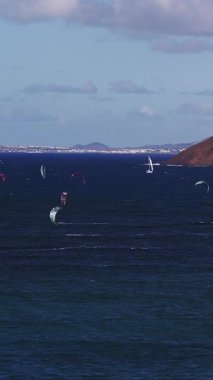 Kanarya Adaları 'ndaki Fuerteventura üzerinde 4K hava manzarası. Uçurtmacılar Atlantik 'in karanlık sularında yüzerler, beyaz iz bırakır, beyaz yelkenli pas rengi bir burnu geçer..