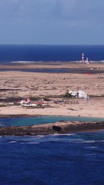 Hava 4K görüntüsü Fuerteventura, Kanarya Adaları 'nı gösteriyor. Kırmızı ve beyaz deniz feneri, Atlantik sörfü, siyah lav kayası, turkuaz lagün, kumlu plaj, uçurtma sörfü ve küçük evler..