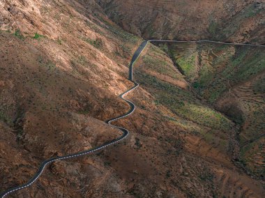 Hava asfalt yolu Fuerteventura, Kanarya Adaları 'ndaki volkanik tepeler boyunca esiyor. Sıkı dönüşler teraslı yamaçlar ve vadiler yumuşak gün ışığında yamalı güneş ve gölgelerle kesilir..