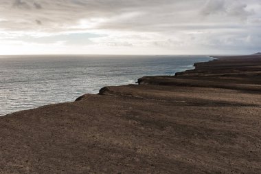 Paslı kahverengi volkanik plato Fuerteventura, Kanarya Adaları 'nda sakin bir Atlantik' e iniyor. Dağınık post fırtına ışığı ve puslu ufuk yalnızlığı ve ölçeklendirmeyi vurguluyor.