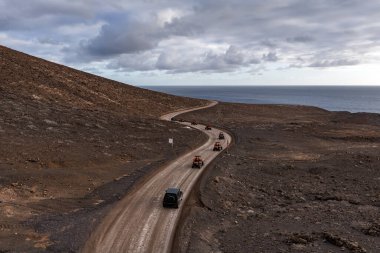 Bir fayton ve 4x4 konvoyu Fuerteventura, Kanarya Adaları 'nda, gün batımında kara kara kara düşünen bulutların altında Atlantik Okyanusu' na doğru yol alır..