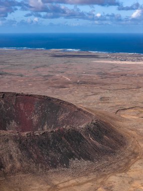Hava görüntüsü Fuerteventura, Kanarya Adaları 'nın yakınında paslı renkli bir külah gösteriyor. Dik kenarları, moloz yolları, düz lav alanları, Atlantik ufku ve küçük bir kıyı yerleşimi var..