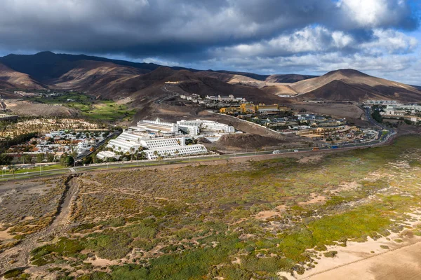 Fuerteventura, Morro Jable yakınlarındaki bir havacılık merkezi. Teraslı oteller lav yamaçlarında yükselir, vadide golf sahası, kıyı yolu etekleri sulu, bulutlar hareket eden gölgeler bırakır..