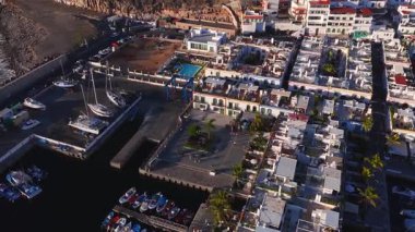 Hava 4K panosu Puerto de Mogan, Gran Canaria 'yı gösteriyor. Marina, Küçük Venedik ızgarası, beyaz evler, yeşil pencereler, otel havuzu, botlar, vinçler, palmiyeler, öğleden sonra ışığı.