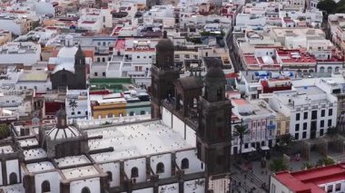 Hava 4K görüntüsü, Las Palmas de Gran Canaria 'da çift volkanik taş kuleler, gül penceresi, beyaz kubbe ve Plaza de Santa Ana' nın palmiyeleri ve yayaları olduğunu gösteriyor.
