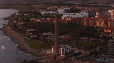 Hava 4K, Faro de Maspalomas 'ı Gran Canaria' daki gezinti güvertesinde gösteriyor. Atlantik solda, tatil beldeleri ve iç kısımlarda. Dalgalar sarmaş dolaş yürürken ve yanan bir Noel ağacı parıldarken kalabalık.