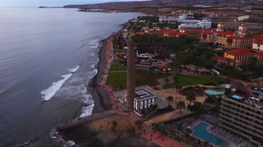 Maspalomas Deniz Feneri, Gran Kanaryası, Palmiye Avuç İçleri, Kırmızı Çatı Otelleri, Kayalık Kıyı, Kumsal, Kalabalık, Gün batımı Işığı, Ufukta Teide.