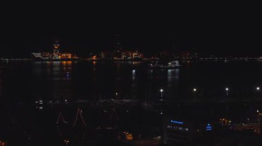 Las Palmas de Gran Canaria 'daki hava sahasında ışıklandırılmış iskele vinçleri, Vithas Hastanesi işareti, parlak gemi yansımaları, durgun su ve şenlik ışıklarıyla marina direkleri görülüyor..