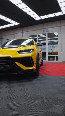 Sarı Lamborghini Urus Performante bir dinlenme atölyesinde oturur ve kamera büyük panel ışıkları altında tampon, tekerlek kemeri ve LED farları yavaş yavaş ortaya çıkarır..