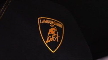 Yavaş bir tavada Lamborghini Urus Performante koltuk amblemi, altın işlemeli ve sarı dikişli kumandalı stüdyo ışıklandırmasında koyu siyah süsleme görünür..