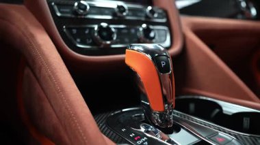 Bentley Bentayga kabini krom teçhizat seçiciyi, karbon fiber konsolu, geniş bilgi toplama ekranını, analog saati, sıcak ışığı, pürüzsüz tavaları ve kapalı alandaki odak çekimleri gösteriyor..