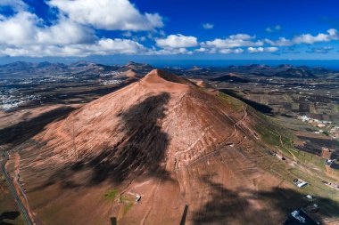 Hava görüntüsü, Timanfaya Ulusal Parkı, Lanzarote yakınlarındaki La Geria 'da Atlantik ufku ve beyaz mezralarıyla birlikte kül külahı, lav tarlaları ve teraslı üzüm bağları gösteriyor..