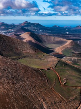 Lanzarote 'deki hava sahnesinde kül konileri, kalderalar, La Geria tarlaları, beyaz köyler ve Atlantik ufku uzun gölgeler ve izler görülüyor..