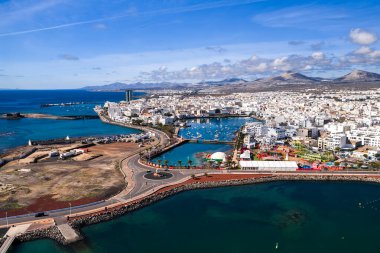 Arrecife, Lanzarote hava sahasında Charco de San Gines 'i küçük teknelerle, beyazlatılmış şehirlerle, volkanik tepelerle, dönme dolaba, çadırlara, Atlantik' e ve dalgakıranlara kadar gezerken gösteriyor..