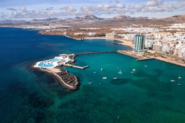 Arrecife, Lanzarote hava görüntülerinde Gran Hotel Arrecife, Lago de Marina ve yaya köprüsü, küçük tekneler, altın plajlar, volkanik tepeler ve beyaz mimariyi gösteriyor..