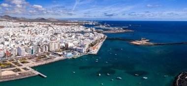 Arrecife, Lanzarote 'nin hava manzarası, Castillo de San Gabriel' e giden turkuaz körfez, liman ve dalgakıran tarafındaki beyaz binaları, gün ışığında küçük tekneleri ve volkanik tepeleri gösteriyor..