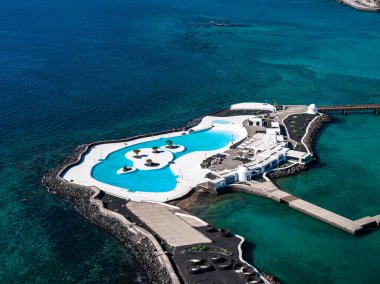 Arrecife, Lanzarote 'deki tuzlu su gölünün havadan görünüşü, beyaz terasları, turkuaz havuzu, adacıkları ve parlak gün ışığı altında kayalık bir dalgakıran üzerinde palmiyeler..