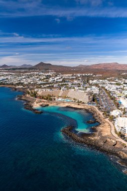 Puerto del Carmen veya Costa Teguise, Lanzarote 'nin havadan görünüşü, lav kıyısı, teraslı otel, küçük plajlar, doğal havuzlar ve kurak volkanik tepeler..