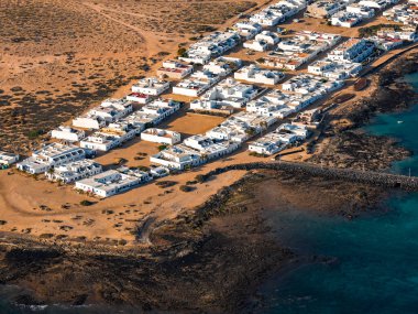 Hava sahnesinde kayalık kıyılarda beyaz kübik evler ve La Graciosa 'da Mirador del Rio yakınlarında Caleta de Sebo ile turkuaz sığlıkları görülüyor. Öğleden sonra ışığı ızgarayı ve kıvrımlı dalgakıranı tanımlar.